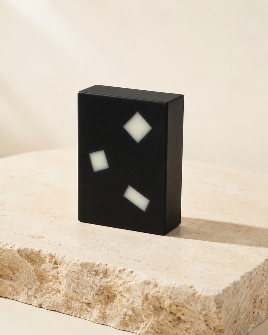 The Charcoal Aloe bar, black with embedded aloe pieces, standing on a travertine ledge