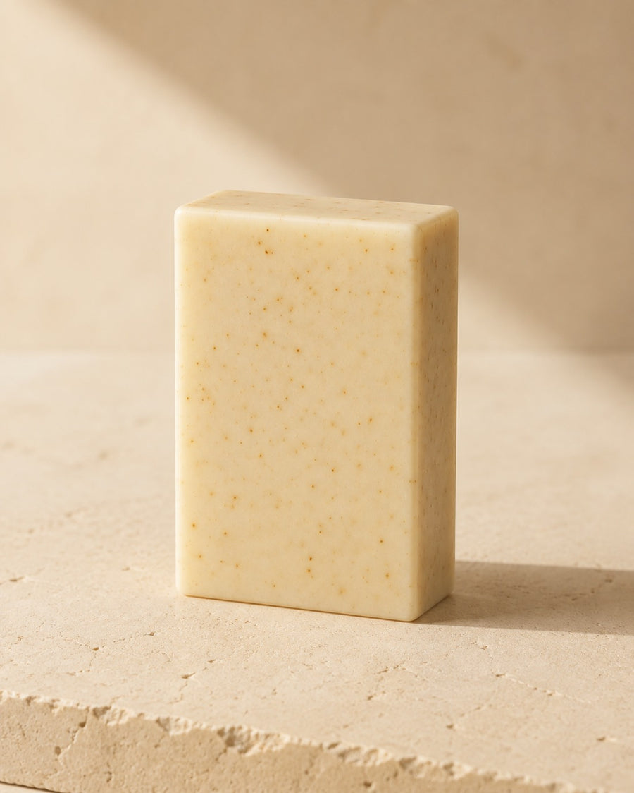 The Grapefruit Tea Tree bar, warm ivory with citrus speckles, standing on a travertine ledge