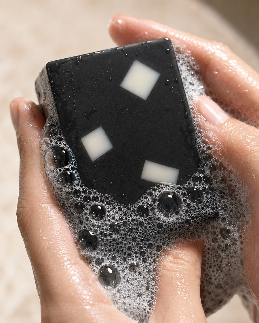 The Charcoal Aloe bar worked into a dense lather between two wet hands