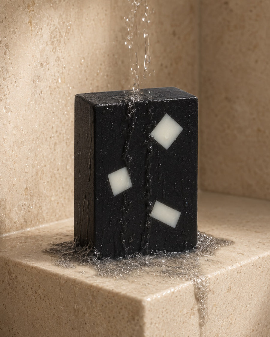 The Charcoal Aloe bar rinsing under running water on a stone shower ledge